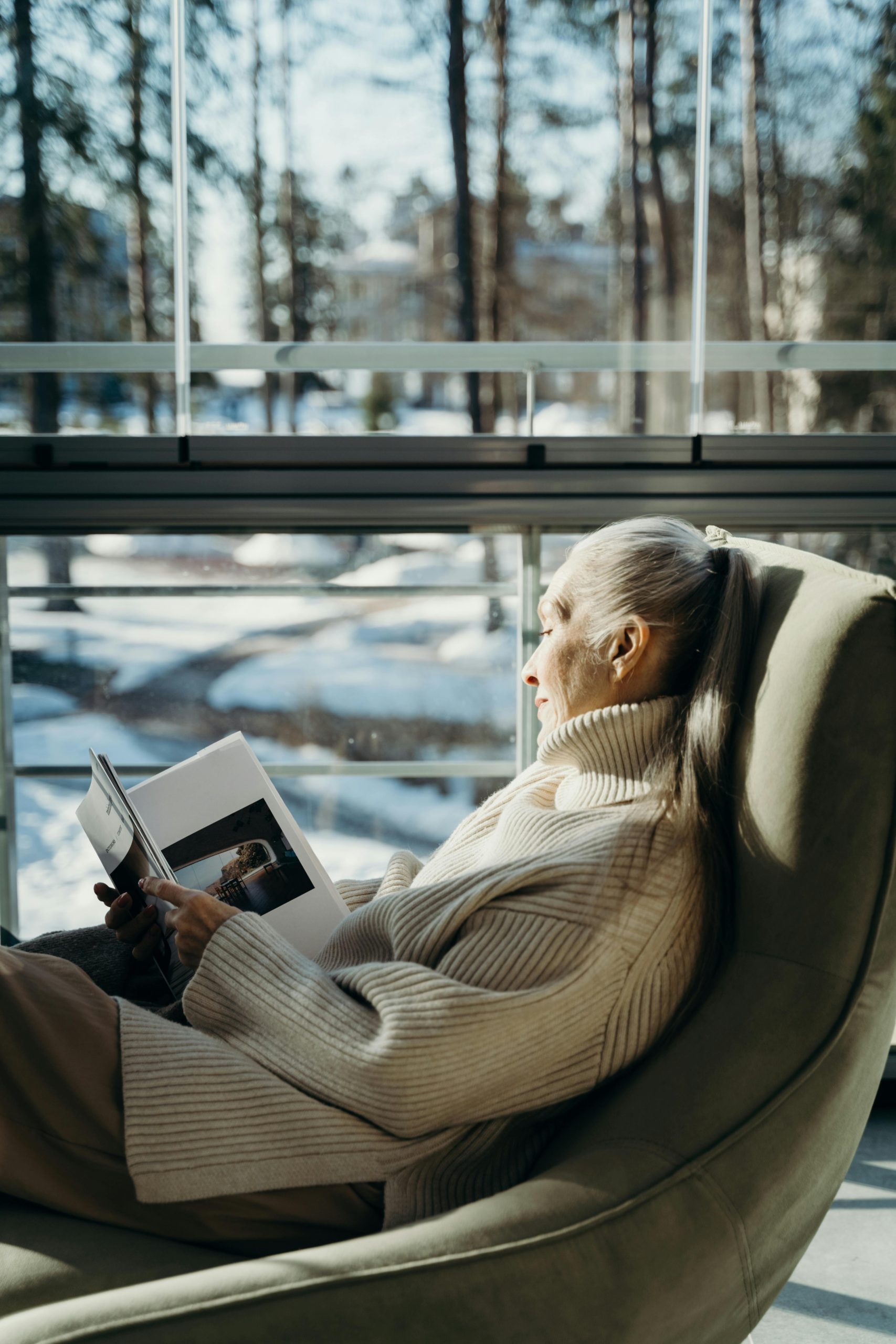 Une retraitée lit une revue tranquillement dans son fauteuil à sa fenêtre